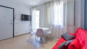 Ein modernes Wohnzimmer mit einem roten Sofa, einem Esstisch mit Stühlen, einem an der Wand montierten Fernseher und einem großen Fenster mit durchsichtigen Vorhängen.
