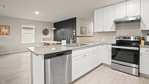Een moderne keuken met roestvrijstalen apparatuur, witte kastjes en een granieten aanrecht.