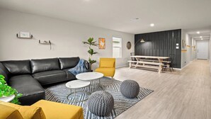 Een moderne woonkamer met een zwarte leren bank, een gele fauteuil en een eethoek met een houten tafel en stoelen.
