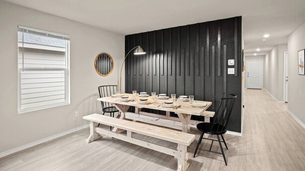 Een eetruimte met een houten tafel voor vier personen, zwarte stoelen, een ronde spiegel en een hanglamp.