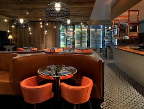 Un restaurante con mesas redondas y sillas anaranjadas, paredes de madera y luces colgantes.