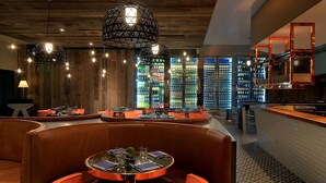 Een restaurant met ronde tafels en oranje stoelen, houten wanden en hangende lampen.