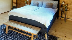 A bedroom with a skylight, a bed with checkered bedding, a bedside table with a lamp, and a bench. - Apartment Chalet Grittelihus, between Interlaken - Gstaad (Diemtigen)