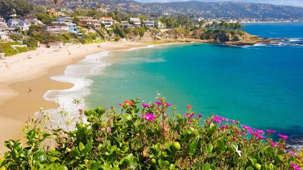 A coastal beach with clear turquoise waters, a sandy shore, and a backdrop of residential buildings. - Vacation Starts Here! Near Irvine Spectrum Center, Pets are Allowed Here (Laguna Hills)