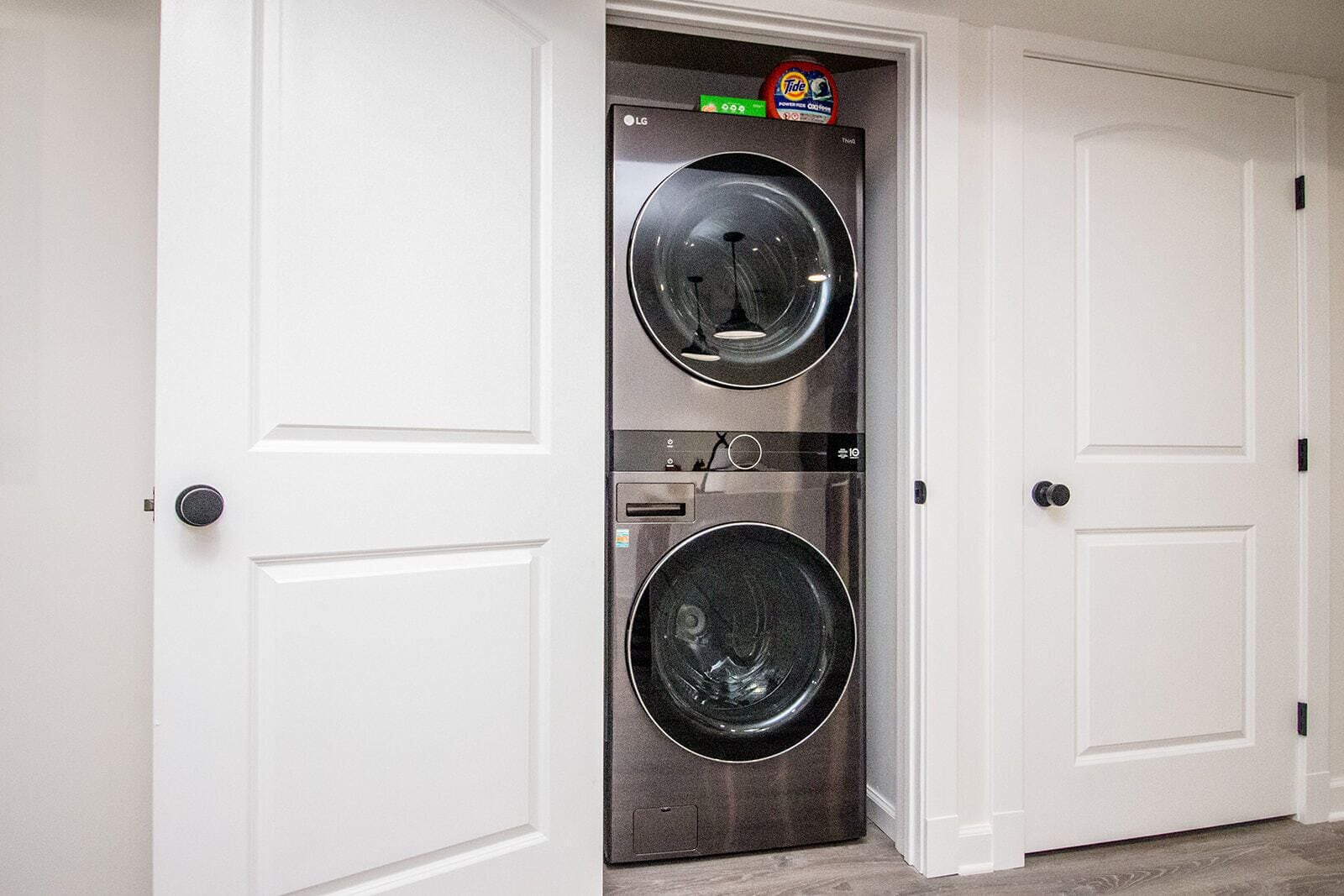 A front view of a laundry room with two stacked front-loading washing machines, white double doors, and a small shelf above the machines.