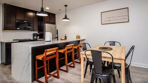 Una cocina moderna con armarios de madera oscura, una isla de mármol y un comedor con mesa y sillas de madera.