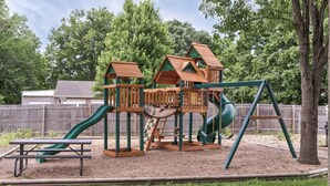 Un parque infantil con una estructura de madera para escalar, toboganes y una mesa de picnic.