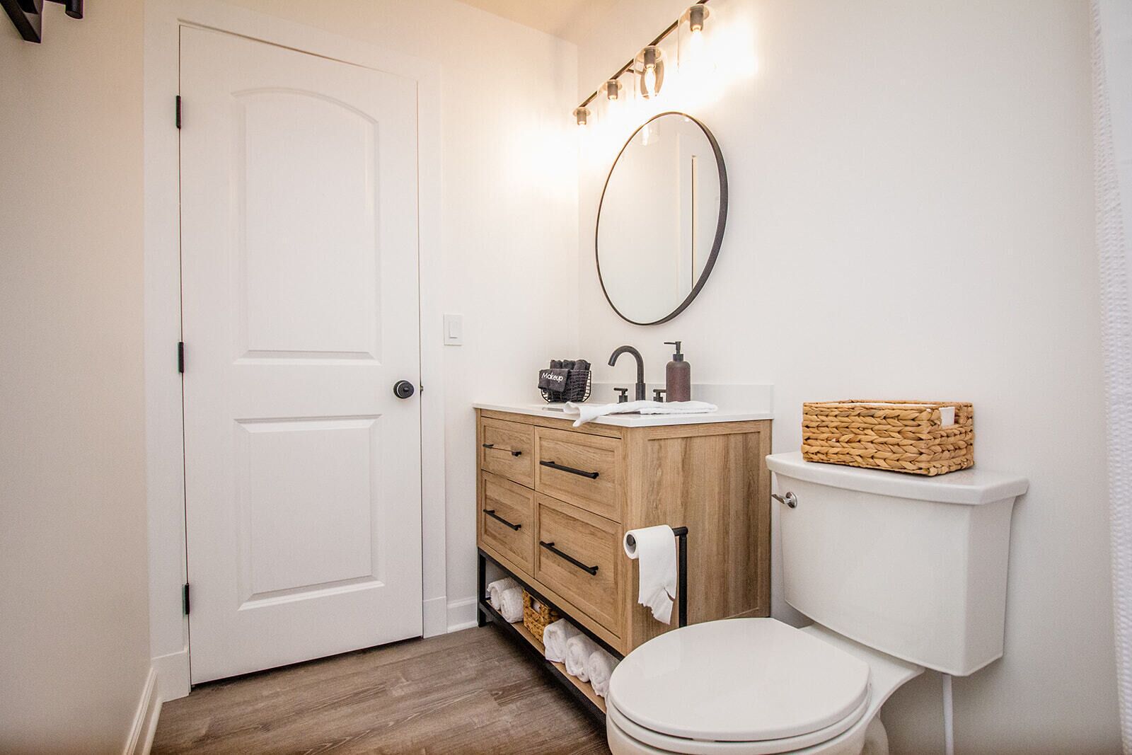 A bathroom with a white toilet, wooden vanity with drawers, a mirror, and a basket on the toilet tank.