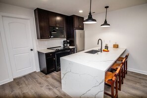 A modern kitchen with dark cabinets, a white marble island, and a black faucet.