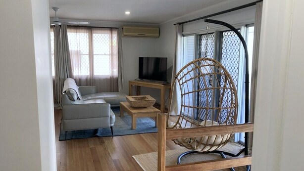 A modern living room with a sofa, a television, a wicker chair, and a small table. - Endeavour Reach (Cooktown)