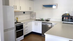 A modern kitchen with white cabinets, a built-in oven, a dishwasher, and a large island. - Endeavour Reach (Cooktown)