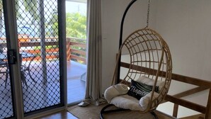 A room with a wicker hanging chair, a sliding glass door leading to an outdoor area, and a wooden floor. - Endeavour Reach (Cooktown)