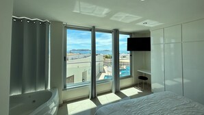 Une chambre d’hôtel moderne dotée d’une grande fenêtre, d’une baignoire, d’un lit et d’un téléviseur fixé au mur.