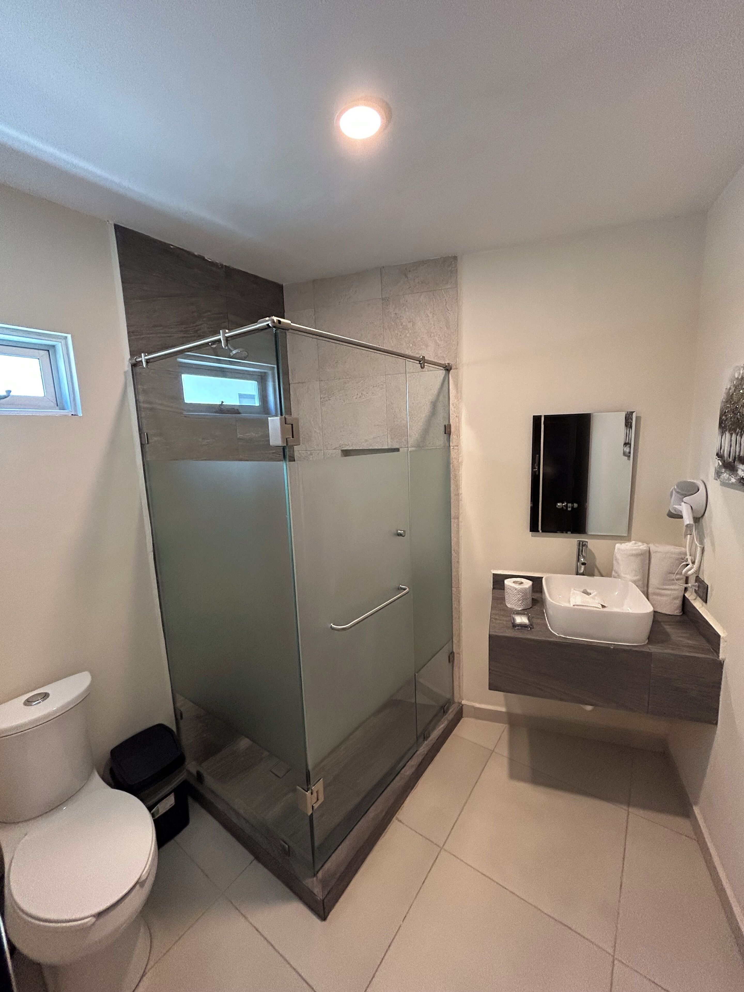 Un baño moderno con ducha de vidrio, inodoro, lavamanos con espejo y un perchero para toallas.