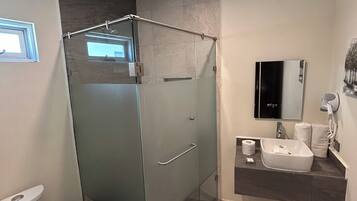 Um banheiro moderno com chuveiro em box de vidro, vaso sanitário, pia com espelho e porta-toalhas.