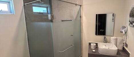 Un baño moderno con ducha de vidrio, inodoro, lavamanos con espejo y un perchero para toallas.