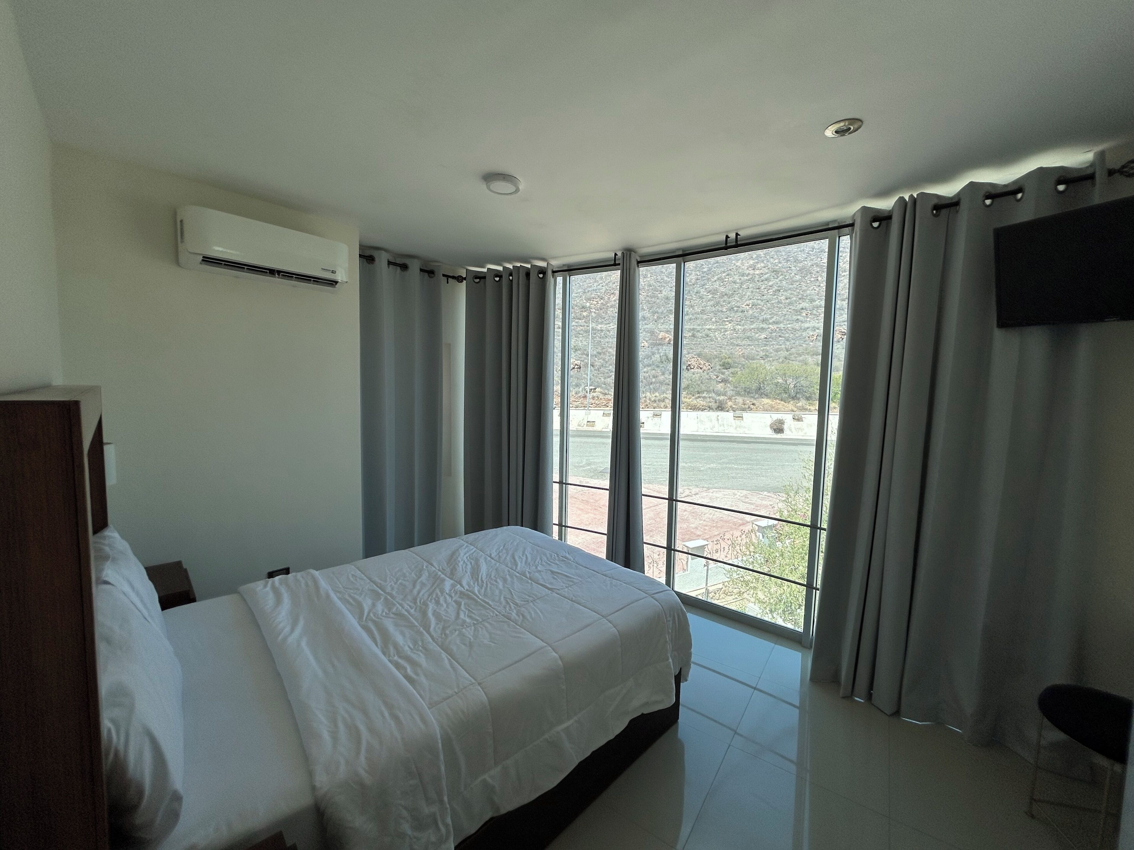 A bedroom with a bed, a TV, and a large window with curtains.