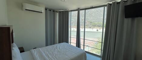 A bedroom with a bed, a TV, and a large window with curtains.