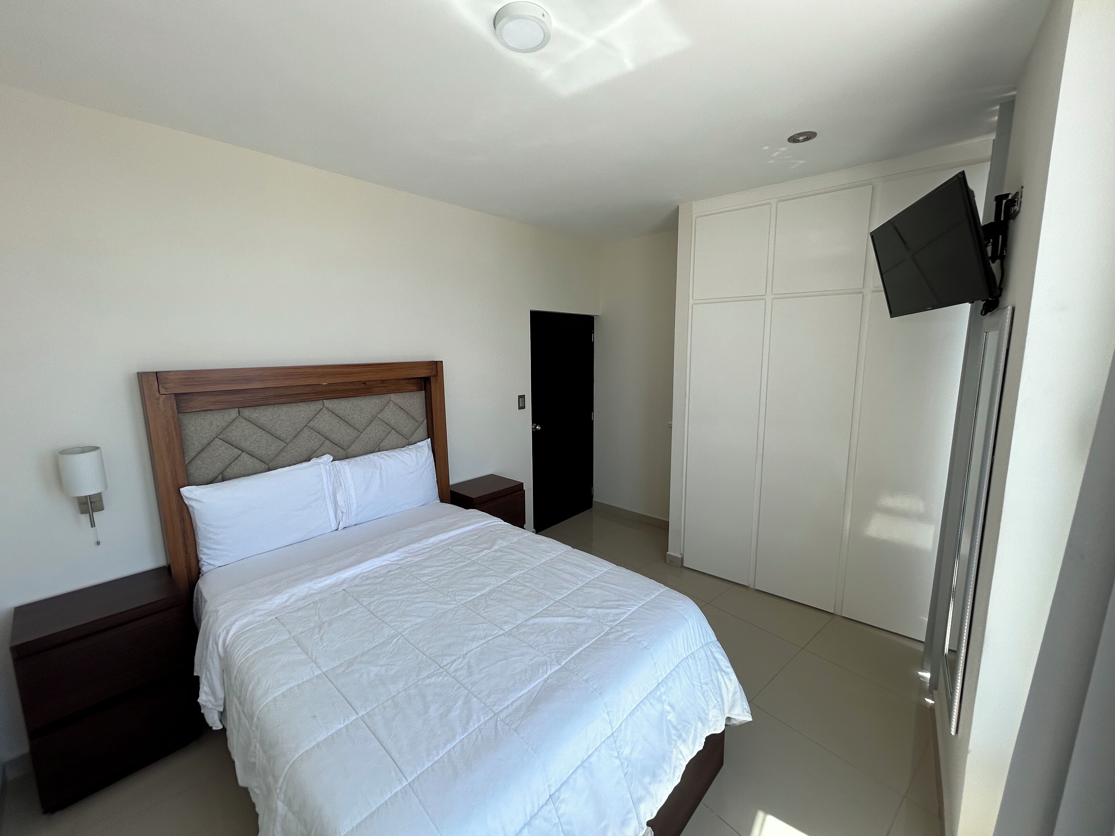 Une chambre d’hôtel équipée d’un lit, d’une table de chevet, d’une armoire et d’un téléviseur fixé au mur.