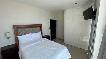 Una camera d'albergo con un letto, un comodino, un armadio e una televisione fissata al muro.
