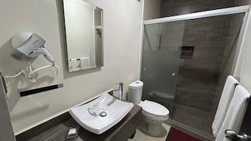 Un baño moderno con lavamanos blanco, secador de pelo, espejo, inodoro y cabina de ducha de vidrio.