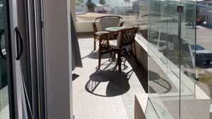 Un balcon doté d’une balustrade en verre, une table avec des chaises et une vue sur la mer et les montagnes.
