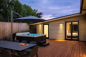 Un patio trasero con jacuzzi, mobiliario exterior y una terraza cubierta.