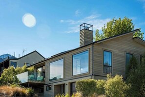 Una casa moderna de dos pisos con ventanas amplias, un balcón y una chimenea.