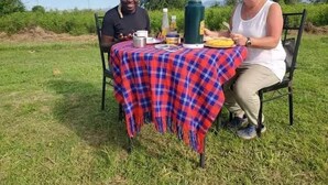 Two people seated at an outdoor table with a red and blue checkered tablecloth, surrounded by greenery.