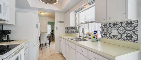 A modern kitchen with white cabinets, a black coffee machine, and a patterned backsplash.