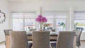 Zona pranzo con tavolo apparecchiato per quattro persone, sedie rivestite in grigio e un vaso con fiori viola.