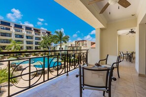 Un balcon donnant sur une piscine, avec des chaises longues et un espace repas comprenant des tables et des chaises.