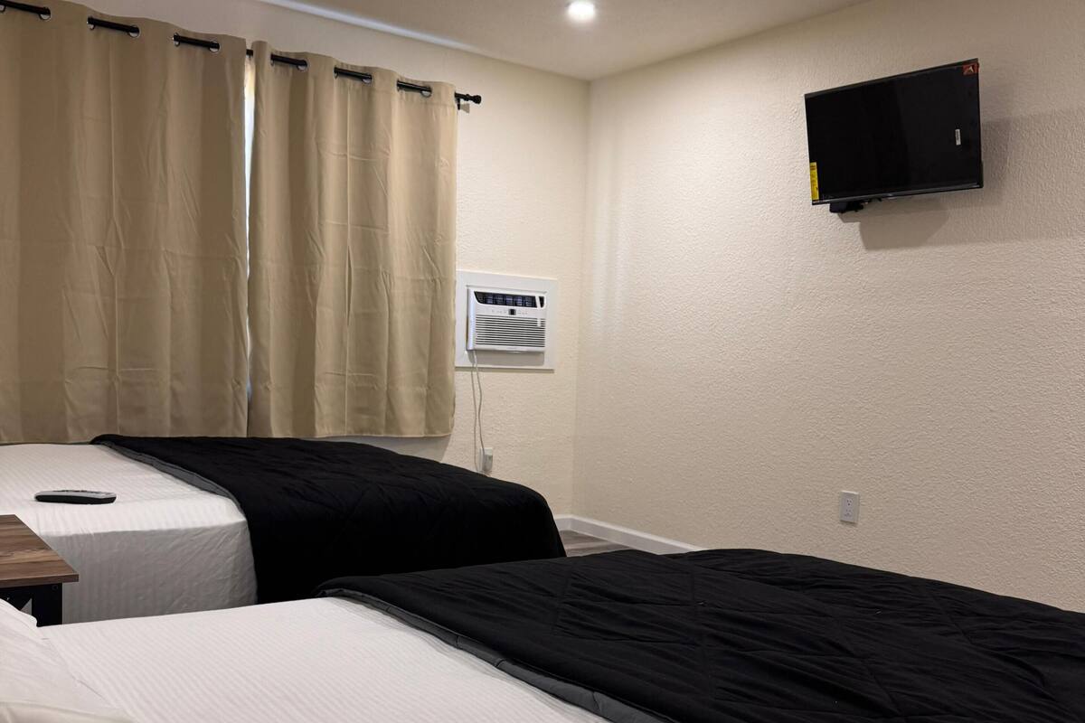 Ein Hotelzimmer mit zwei Betten, einem an der Wand befestigten Fernseher und einer Klimaanlage.