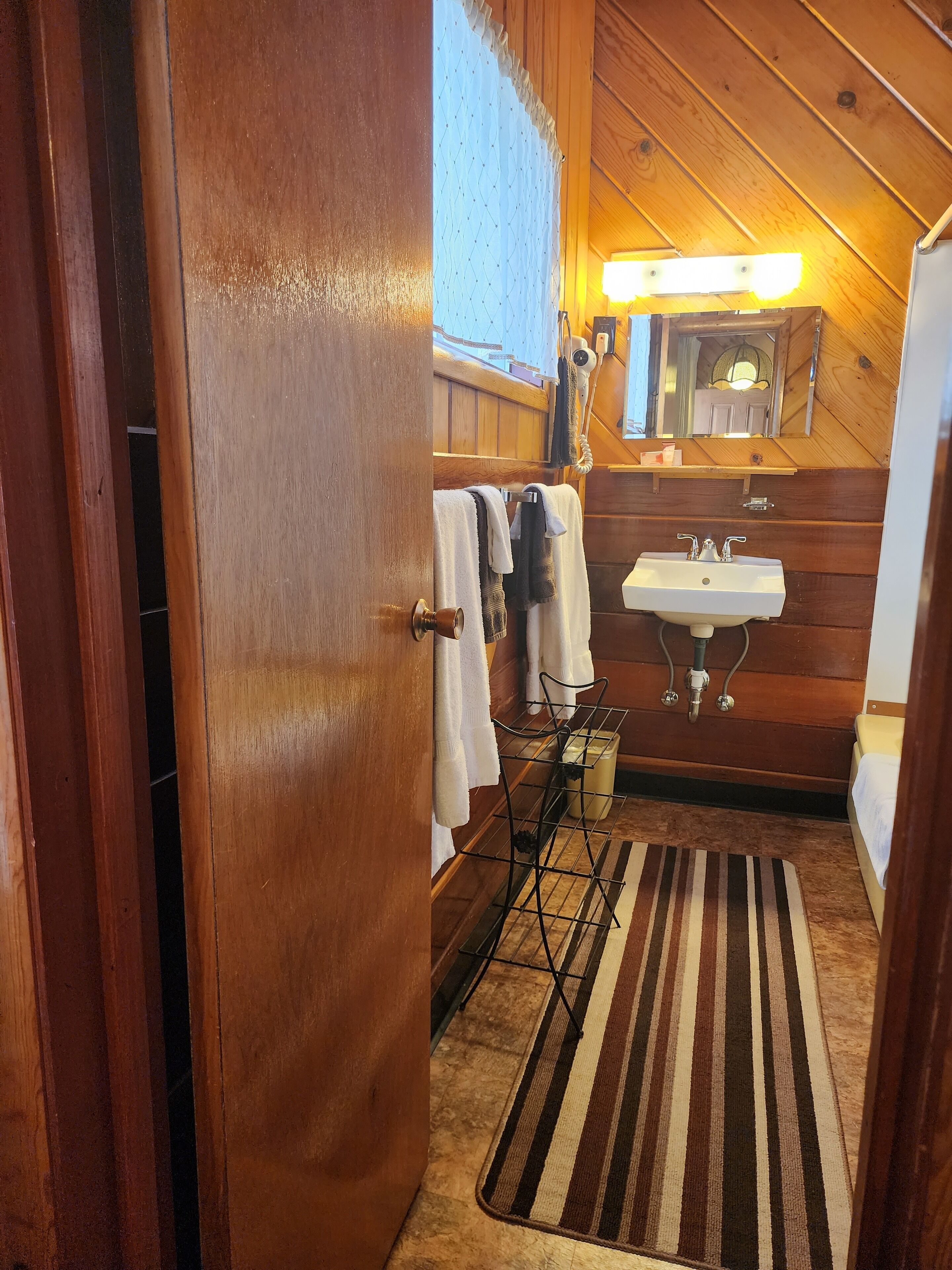 A wooden interior bathroom with a sink, towel rack, and a striped rug.
