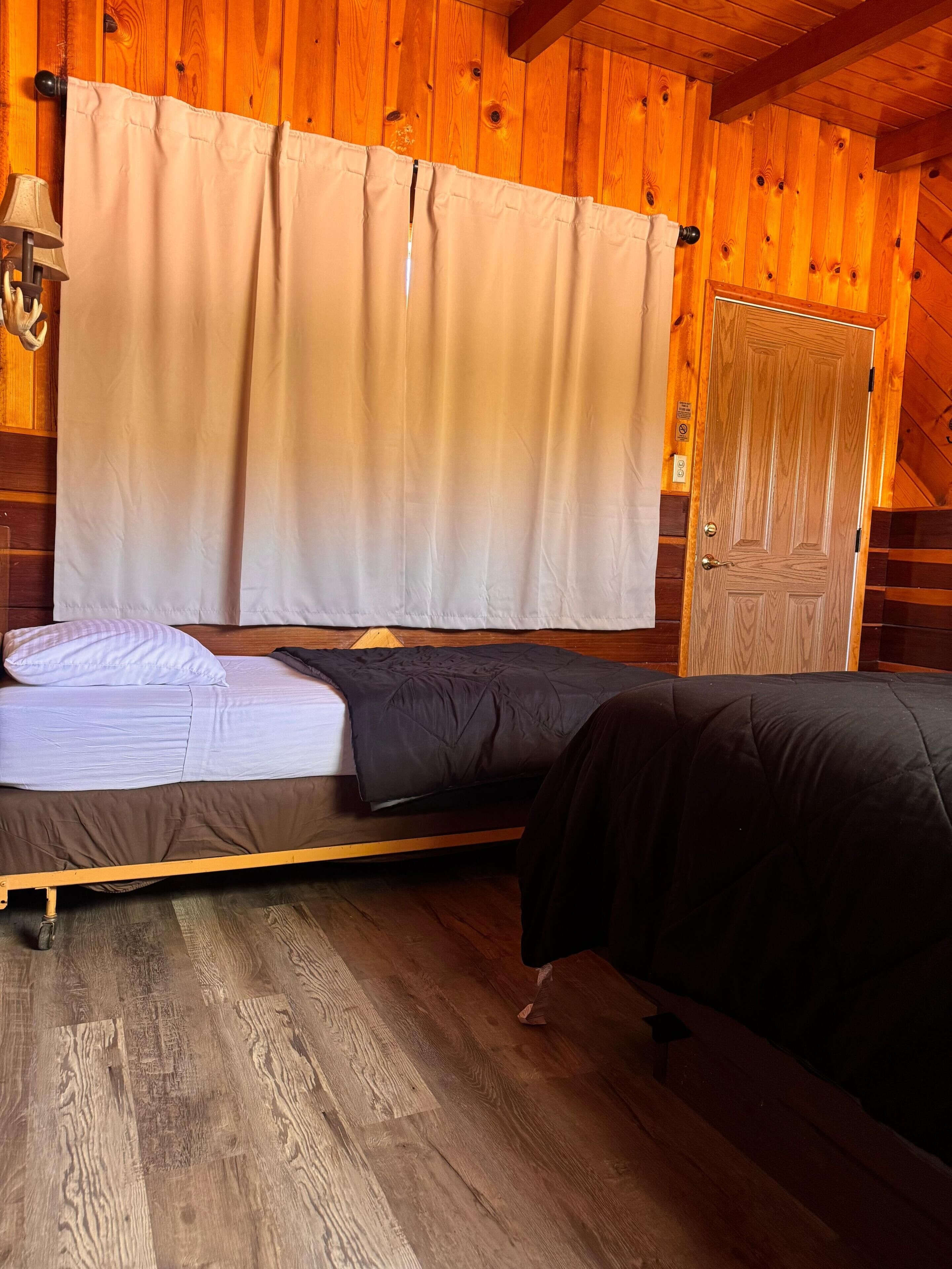 A wooden cabin room with two beds, a wooden floor, and a door.