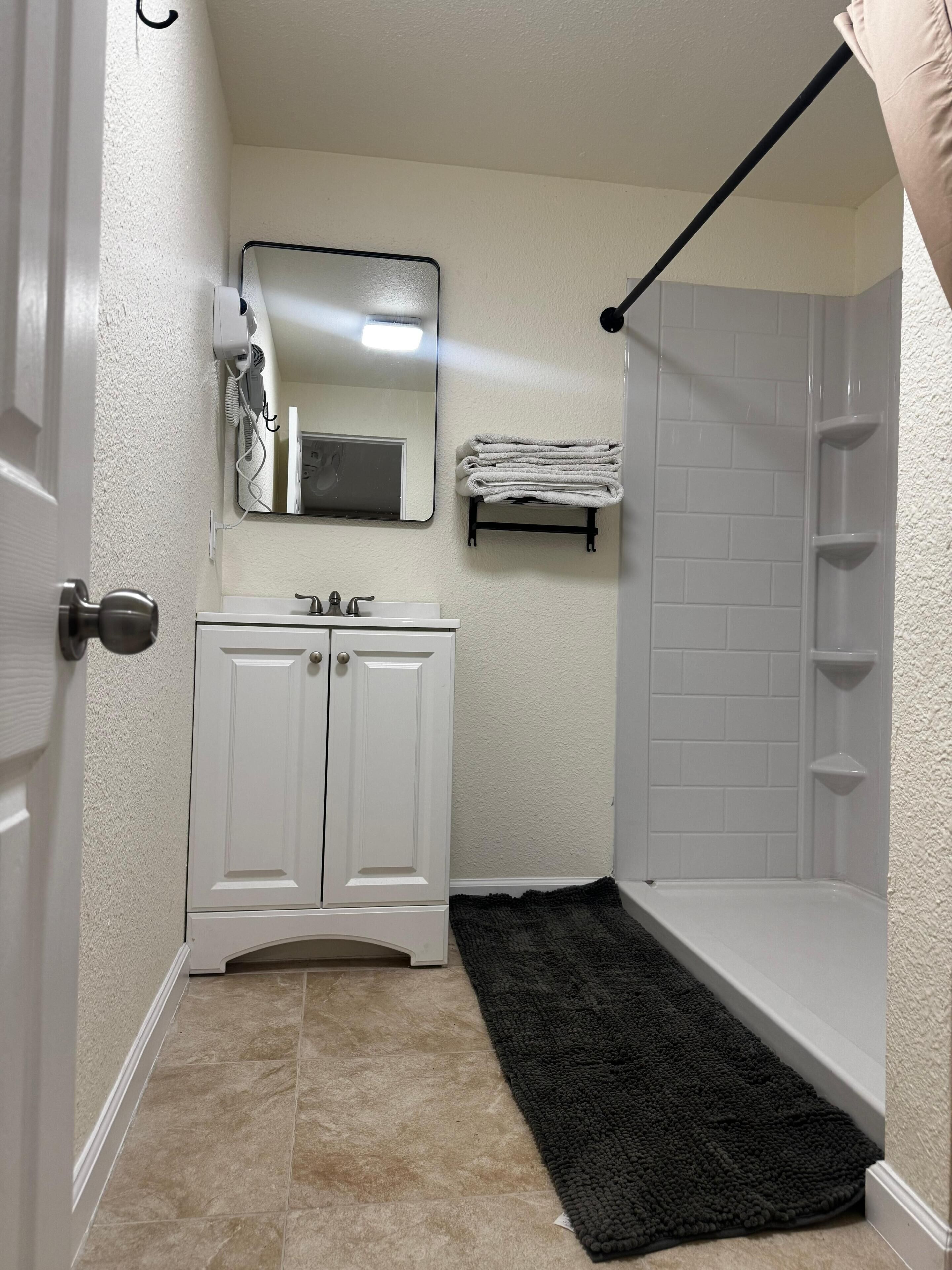 A bathroom with a white vanity, a mirror, a towel rack, and a shower.