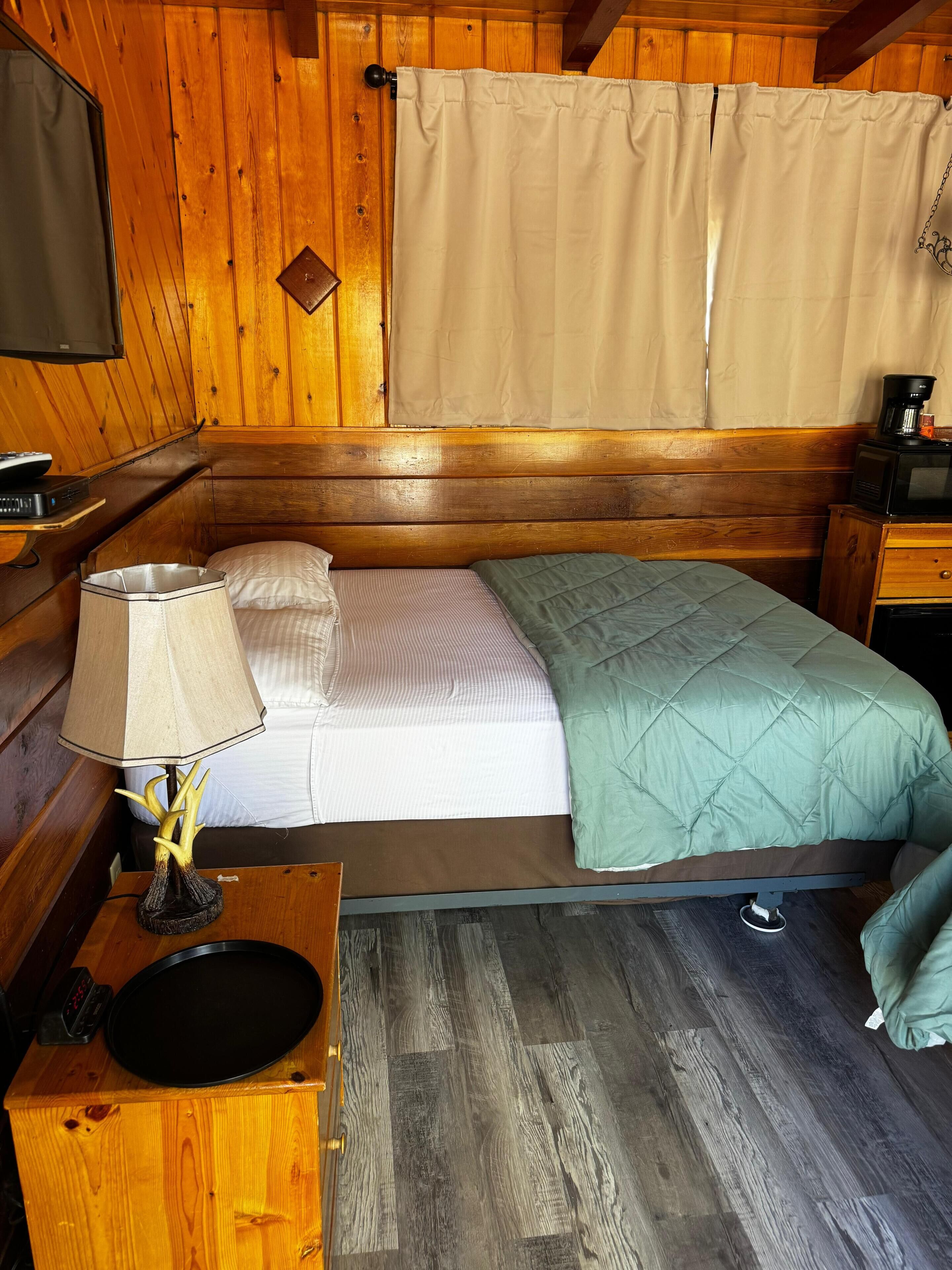 A wooden cabin room with a bed, a lamp, a television, and a microwave.
