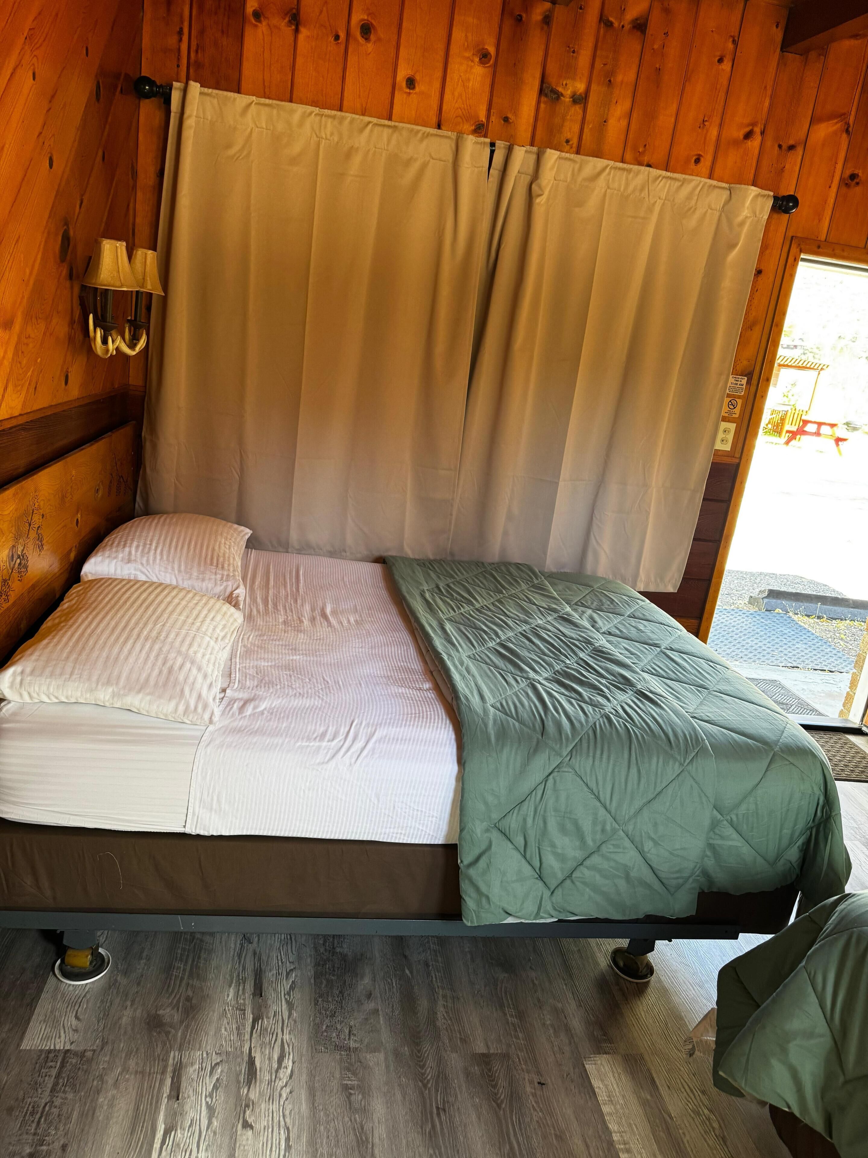 A wooden cabin bedroom with a bed, curtains, and a window.