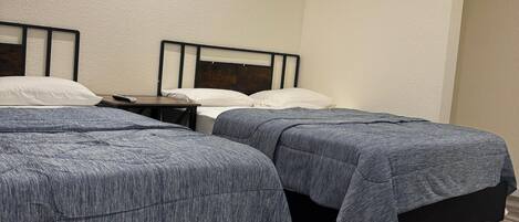 Dos camas individuales con cabeceros de madera y ropa de cama gris en una habitación con suelo de madera y paredes blancas.