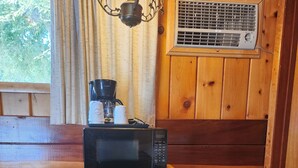 Uma cozinha compacta com micro-ondas, um frigorífico pequeno e uma máquina de café, tudo sobre um armário de madeira.