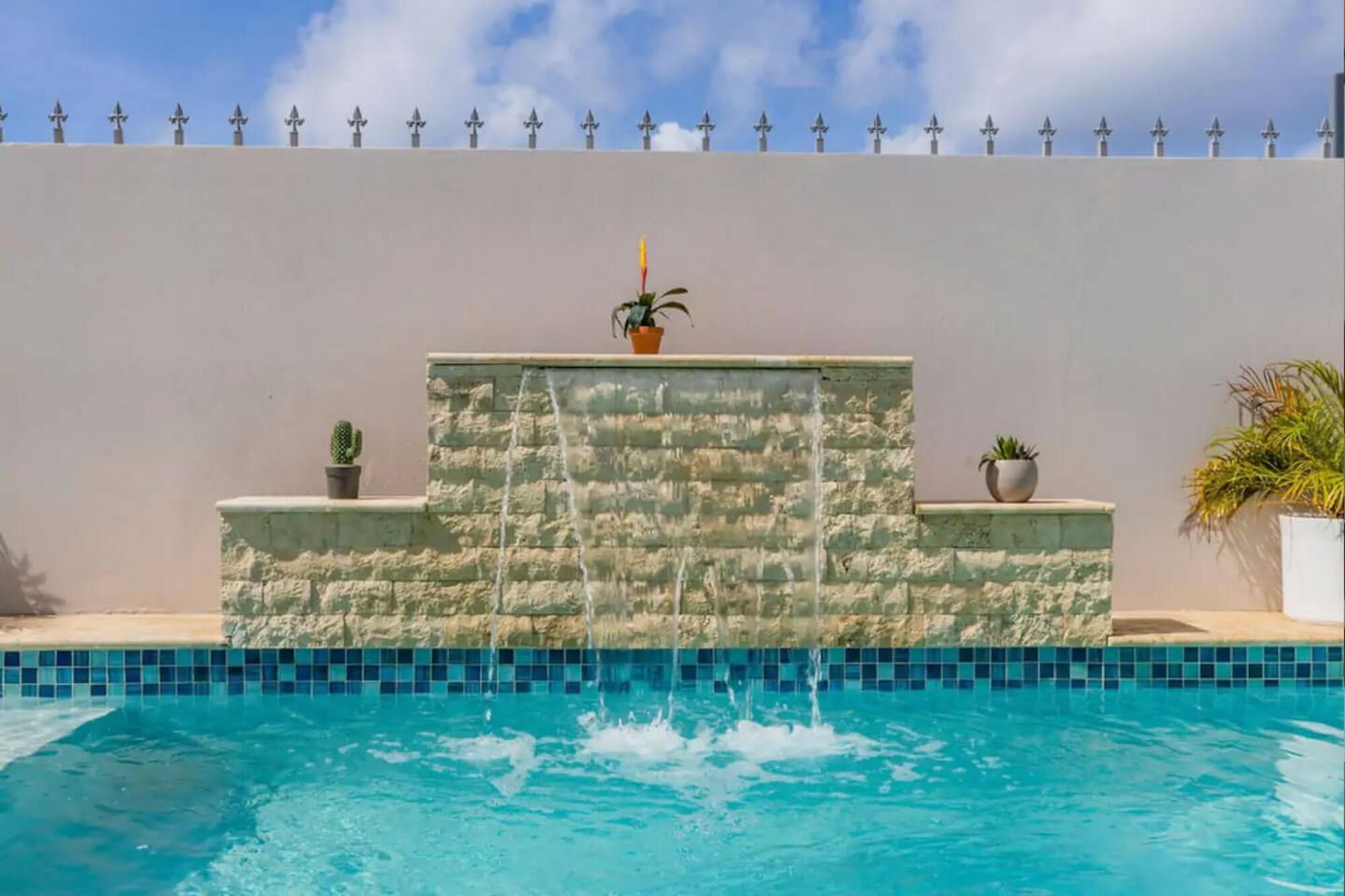 A swimming pool with a stone wall and potted plants.