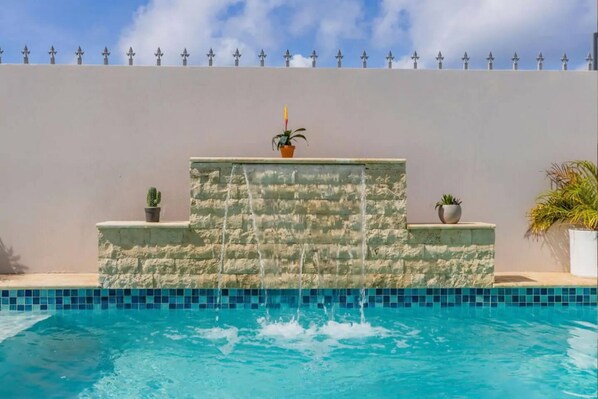 A swimming pool with a stone wall and potted plants.