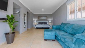A modern bedroom with a bed, bedside tables, a blue sofa, a potted plant, and a TV mounted on the wall. - Remodeled 6BR - Privatepool Gameroom Close2beach (Oranjestad)