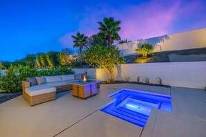 An outdoor patio with a fire pit, seating area, and a hot tub.