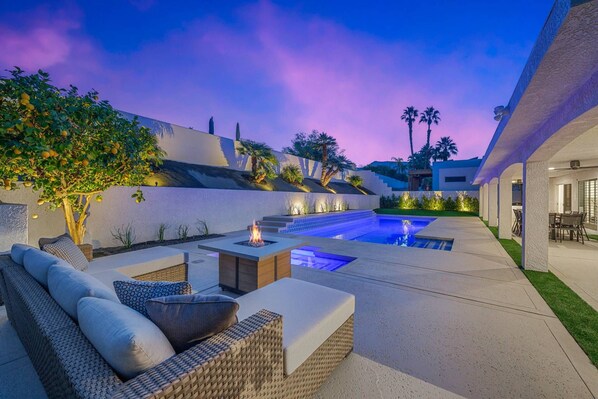 A modern outdoor pool area with a fire feature, seating, and a well-maintained garden.