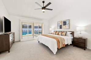 Un dormitorio con cama, televisor, ventilador de techo, mesita de noche y vista a una piscina.
