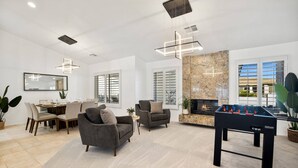 A modern living room with a foosball table, comfortable seating, a fireplace, and large windows. - Palm Desert Home w/Pool & Spa, Walk to Ironwood Park (Palm Desert)
