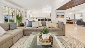 A spacious living area with a large sofa, a coffee table with a plant, and a kitchen in the background. - Palm Desert Home w/Pool & Spa, Walk to Ironwood Park (Palm Desert)