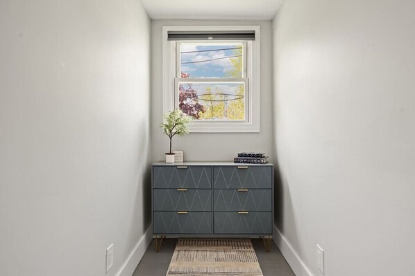 A narrow hallway with a grey cabinet, a small potted plant, and a framed picture above a window.