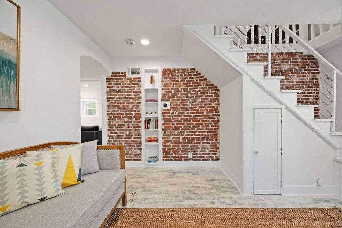 Un salon avec un mur en briques, un escalier blanc, un canapé et une bibliothèque.